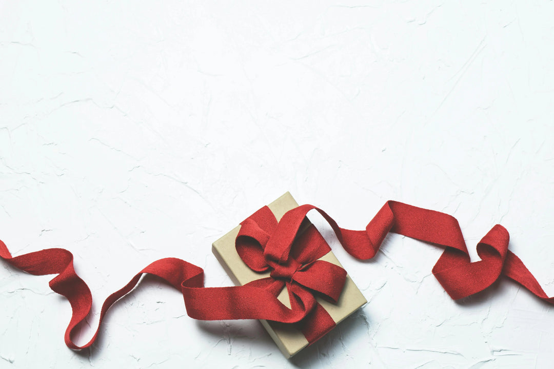 Boîte cadeau beige, ruban rouge, fond texturé blanc.