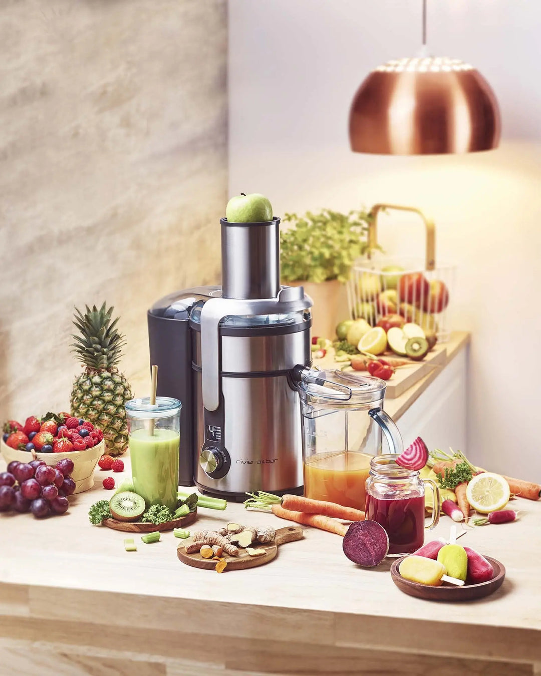 Image de produit: un extracteur de jus Riviera & Bar entouré de fruits et légumes frais, avec des jus de différentes couleurs.