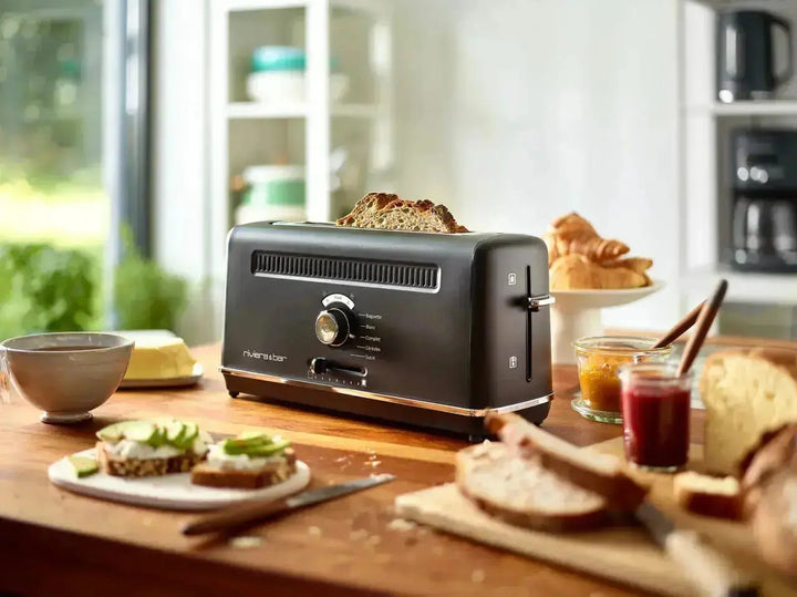 Toaster noir Riviera et Bar sur une table en bois avec pain, confitures, croissants et café.