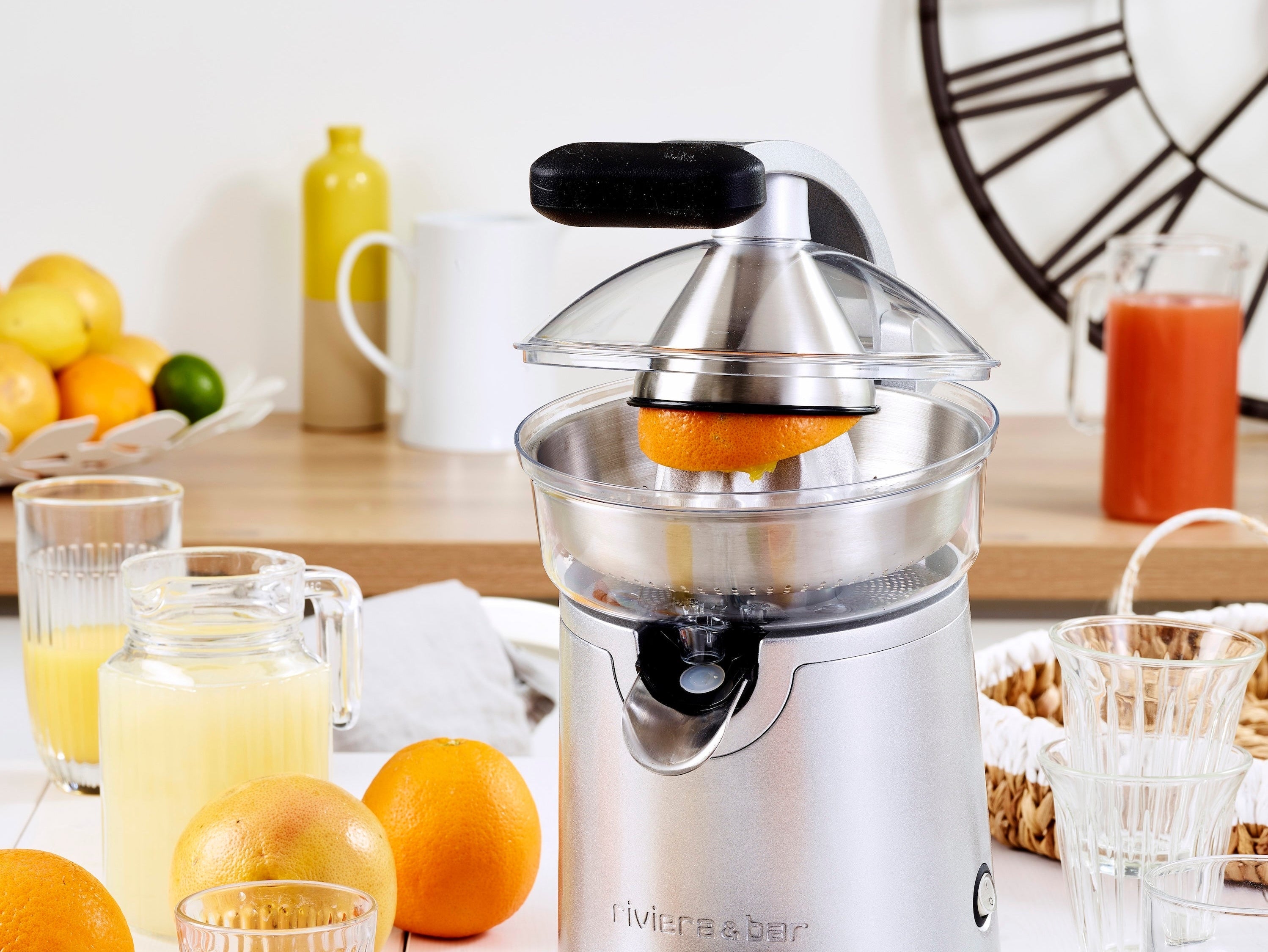 Presse-agrumes riviera&bar en inox avec oranges fraîches et jus versé dans un verre