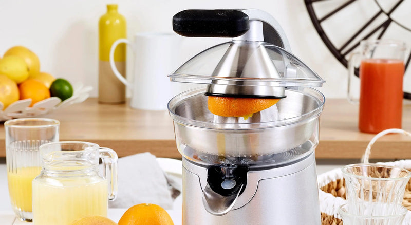 Presse-agrumes riviera&bar en inox avec oranges fraîches et jus versé dans un verre