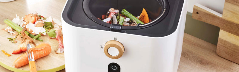 Réducteur de biodéchets riviera&bar posé sur un plan de cuisine moderne avec épluchures de légumes