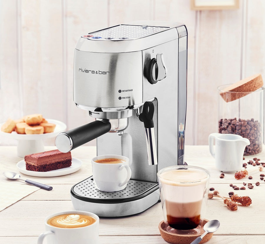 Une machine à expresso argentée trône sur une table en bois, tandis que des cappuccinos, des expressos, des boissons à base de café allongé, des pâtisseries et des grains de café se trouvent à proximité, créant ainsi une scène de petit-déjeuner confortable.