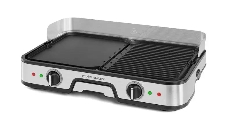 La plancha-gril Combiné riviera&bar se caractérise par un design en acier inoxydable, deux plaques en aluminium (plancha plate à gauche, gril strié à droite), deux boutons de commande, des voyants lumineux et une protection transparente contre les éclaboussures à l'arrière.