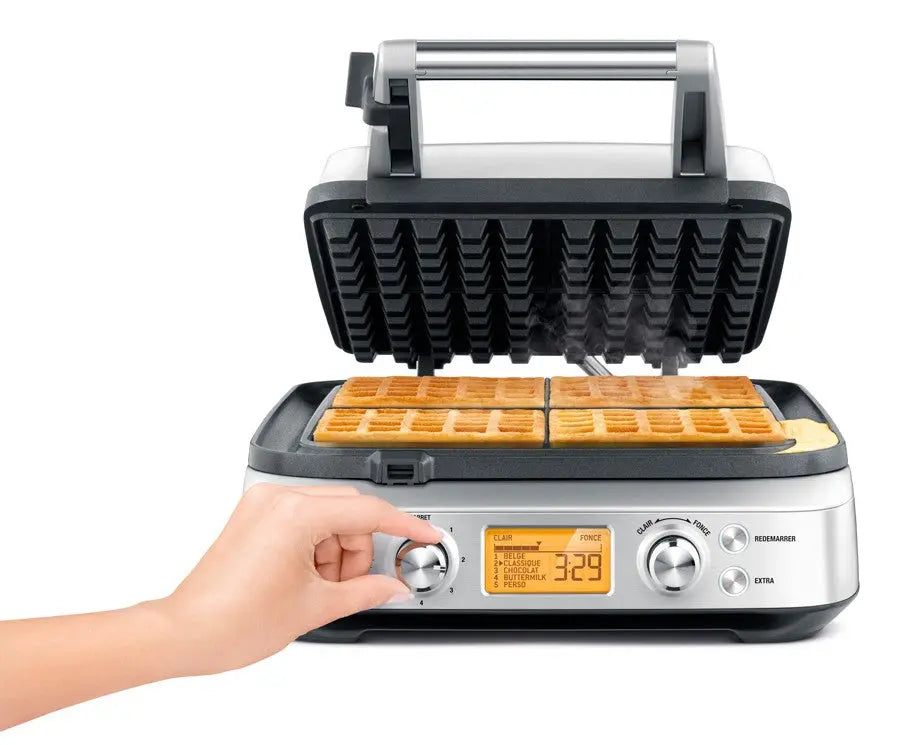 Gaufrier ouvert avec gaufres cuites, main ajustant les réglages.