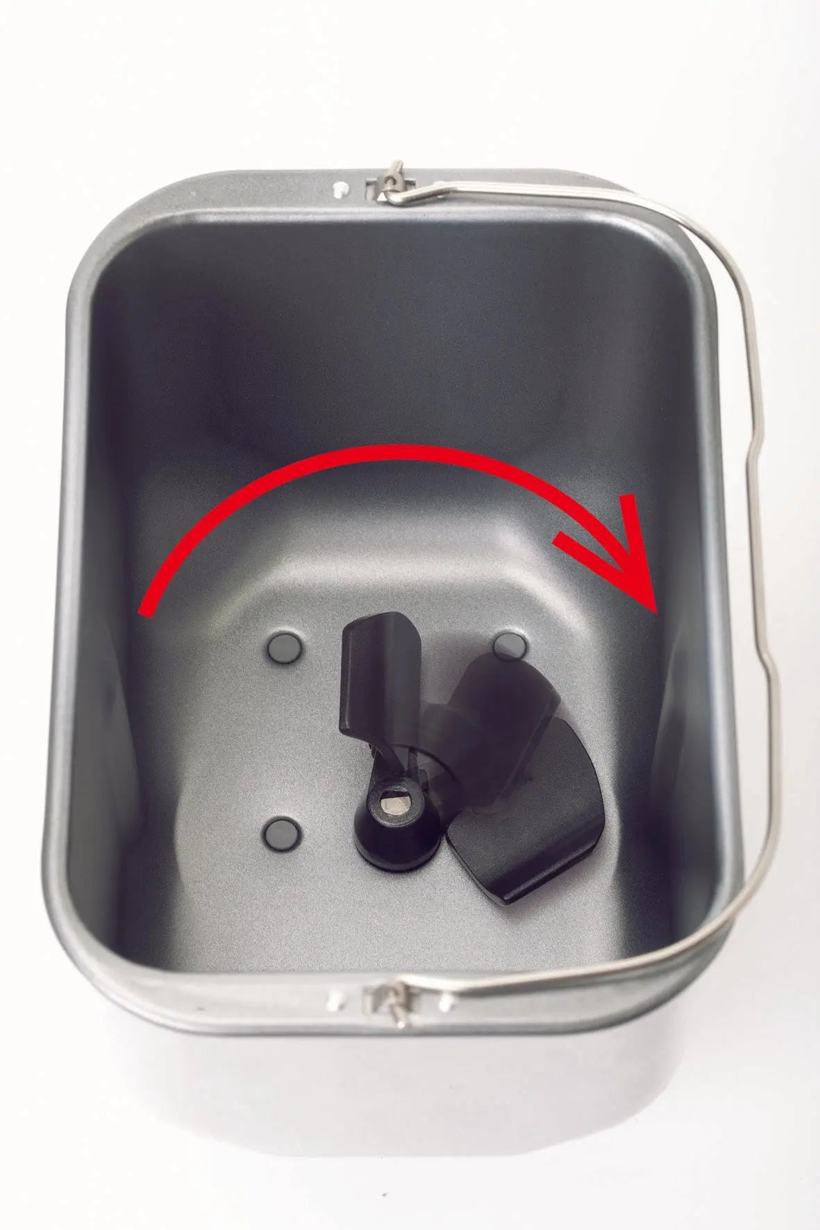 Un moule à pain de la riviera&bar Machine à pain inox Sans gluten & Co - QMP 660 est montré d'en haut, avec une palette en inox à l'intérieur. Une grande flèche rouge s'incurve dans le sens des aiguilles d'une montre au-dessus de la palette, indiquant son sens de rotation.