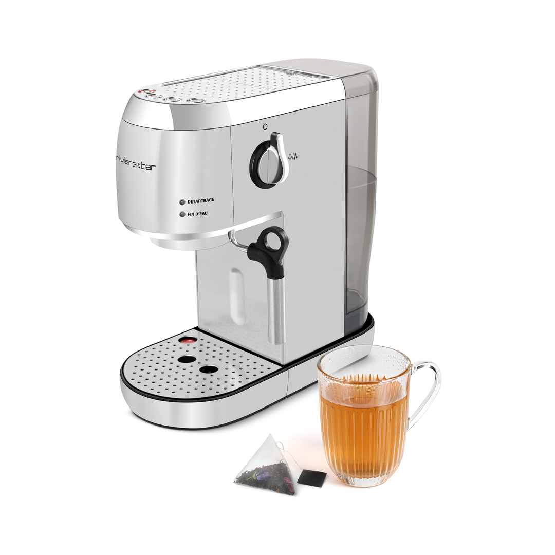 Un Expresso Compact Automatique argenté et blanc de riviera&bar se trouve à côté d'un verre de thé avec un sachet de thé triangulaire, imitant une élégante machine à espresso avec sa puissante pompe à 19 bars.