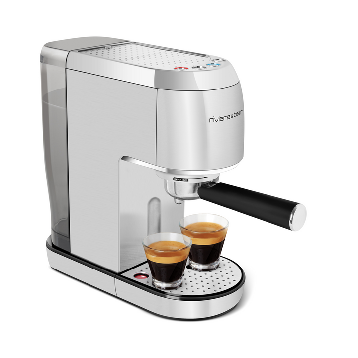 L'Expresso Compact Automatique de riviera&bar est une machine à espresso argentée avec une poignée noire, utilisant du café moulu pour préparer deux tasses à la fois. Elle est équipée d'une pompe de 19 bars, d'un réservoir d'eau à l'arrière, d'un plateau d'égouttage et d'un design moderne et élégant.