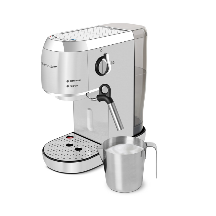 L'Expresso Compact Automatique argenté de riviera&bar, doté d'une pompe à 19 bars, d'une lance à vapeur, d'un réservoir d'eau pour le café moulu et de boutons de commande, est placé à côté d'un pichet à mousse en acier inoxydable rempli de lait mousseux.