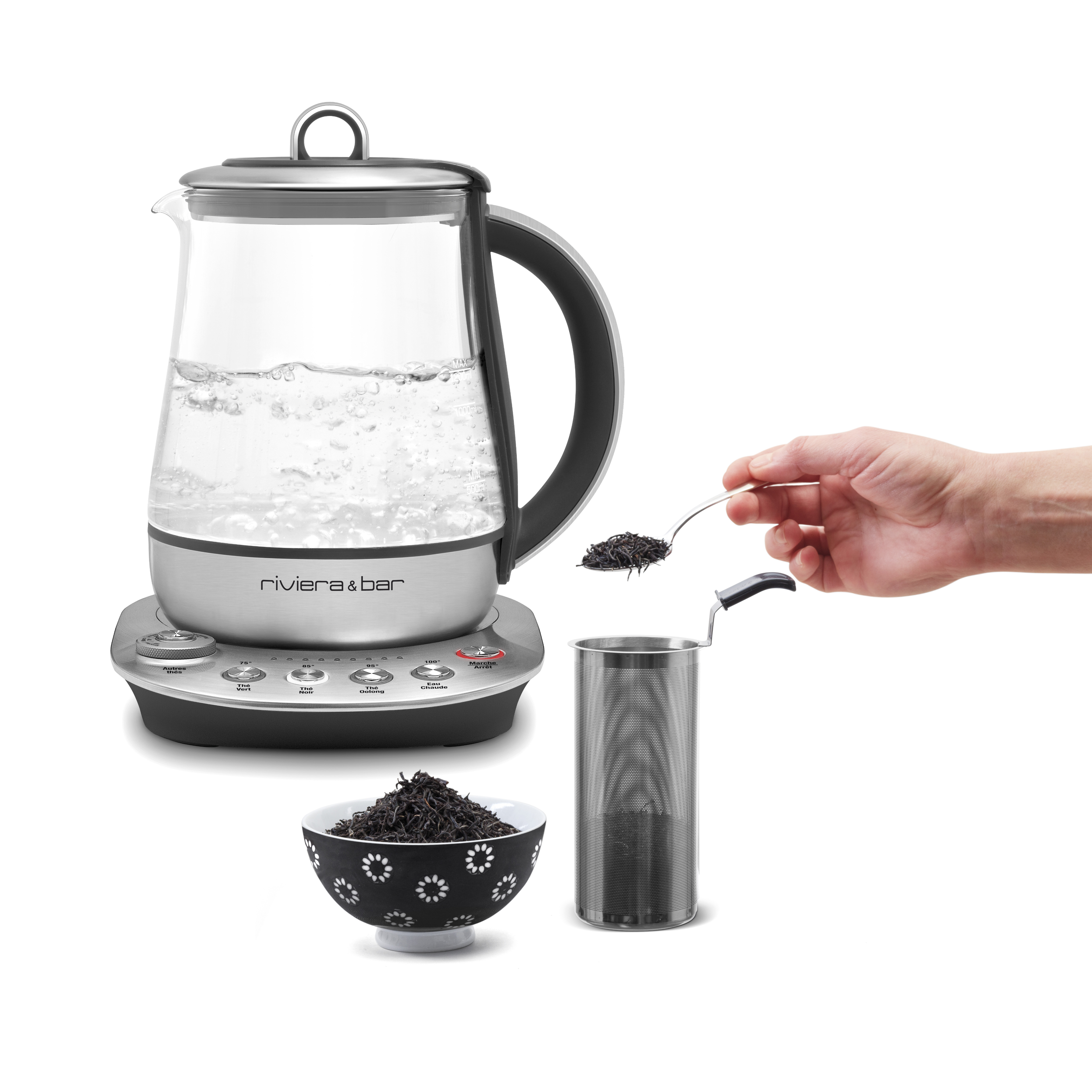 Une Théière Darjeeling Zen électrique programmable riviera&bar est posée sur sa base avec des réglages de thé prédéfinis, tandis que des feuilles de thé en vrac sont introduites à la cuillère dans l'infuseur en métal au-dessus d'un bol noir et blanc.