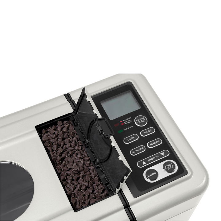 Gros plan de la riviera&bar Machine à Pain Sans gluten & Co MP579A avec un compartiment ouvert rempli de pépites de chocolat, à côté d'un panneau de contrôle comprenant des boutons de programmation et un affichage numérique pour les options sans gluten.