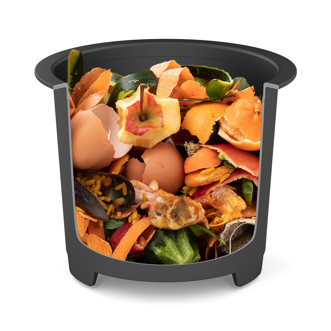 Le Composteur de cuisine Minska de riviera&bar, en noir, est rempli d'épluchures de fruits, de légumes, de coquilles d'œufs et de déchets alimentaires - parfait pour une cuisine zéro déchet. Isolé sur un fond blanc.