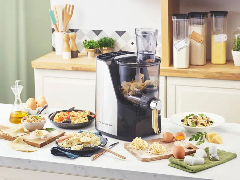 La Machine à pâtes PMP 500 de riviera&bar est posée sur un comptoir de cuisine avec des pâtes fraîches, des œufs, de la farine, de l'huile et des pâtes préparées - idéal pour obtenir une texture parfaite. Des ustensiles de cuisine, des bocaux et des récipients apparaissent en arrière-plan.