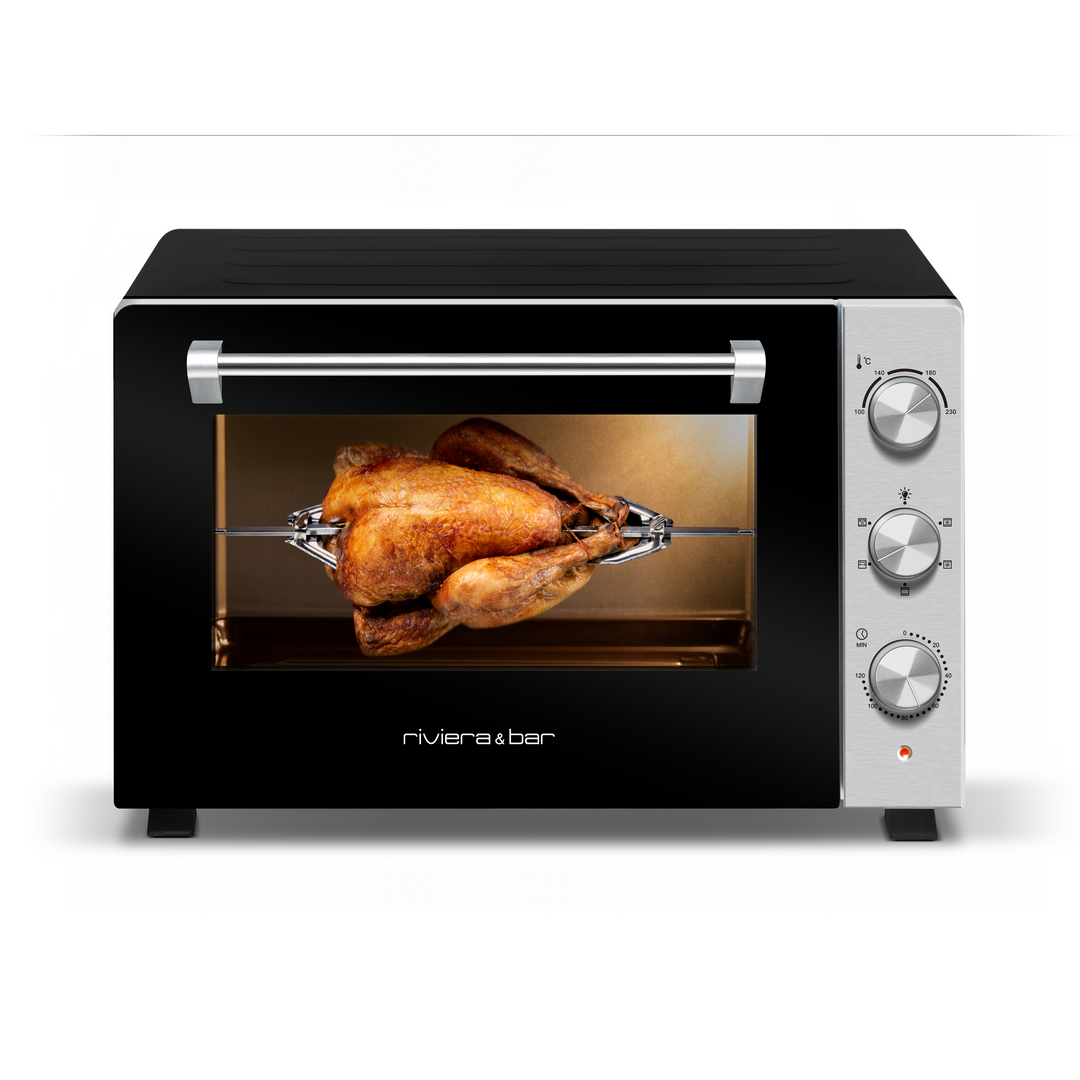 Un poulet rôti entier cuit sur la rôtissoire à l'intérieur du riviera&bar Four posable à parois tempérées 46 L. Ce four de comptoir a une façade noire, des cadrans argentés, une grande fenêtre de visualisation, quatre parois tempérées, et de multiples modes de cuisson.