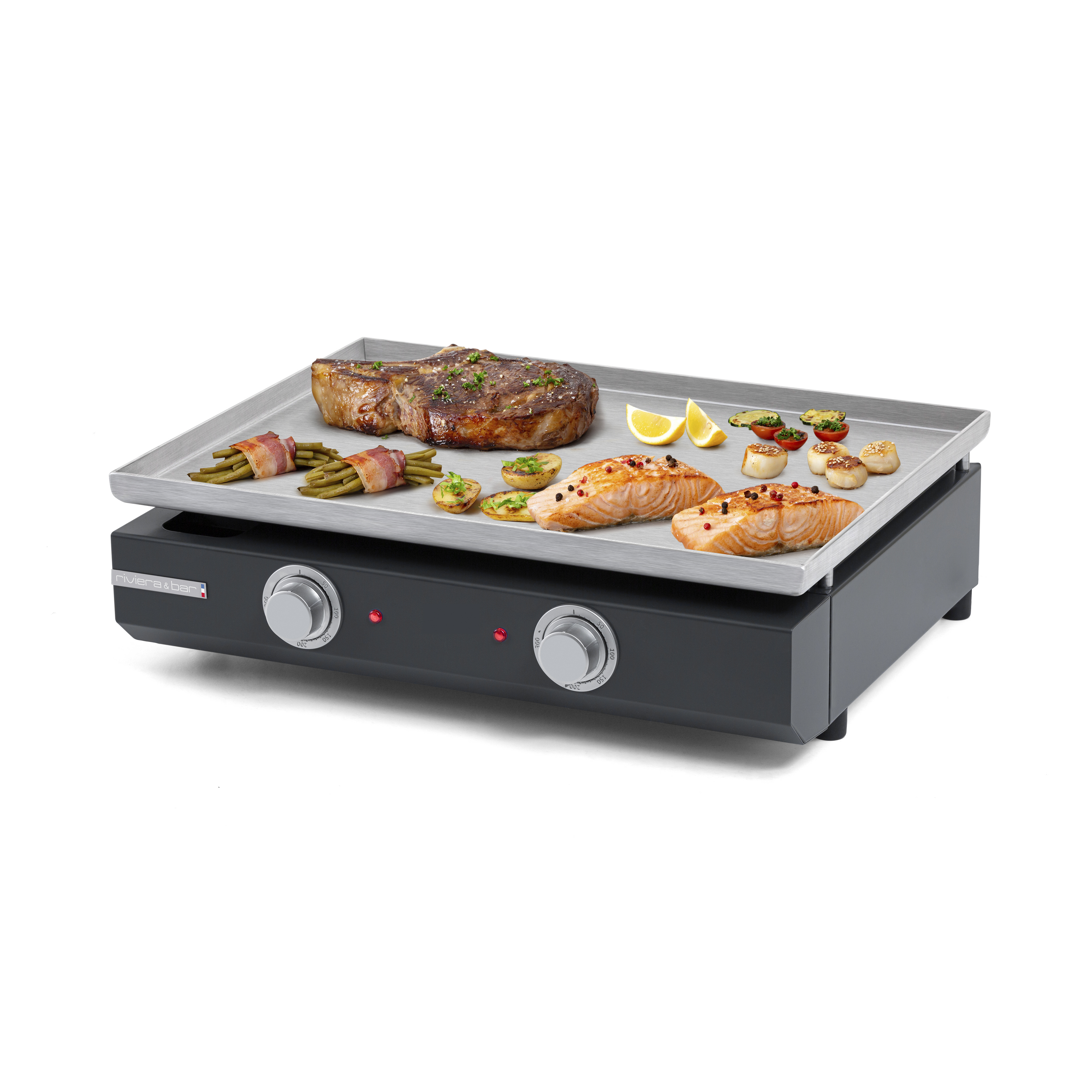 La Plancha électrique longue riviera&bar présente une surface rectangulaire en inox qui grésille avec du steak, du saumon, des légumes, des asperges enrobées de bacon et des quartiers de citron ; deux boutons de commande sont situés à l'avant.