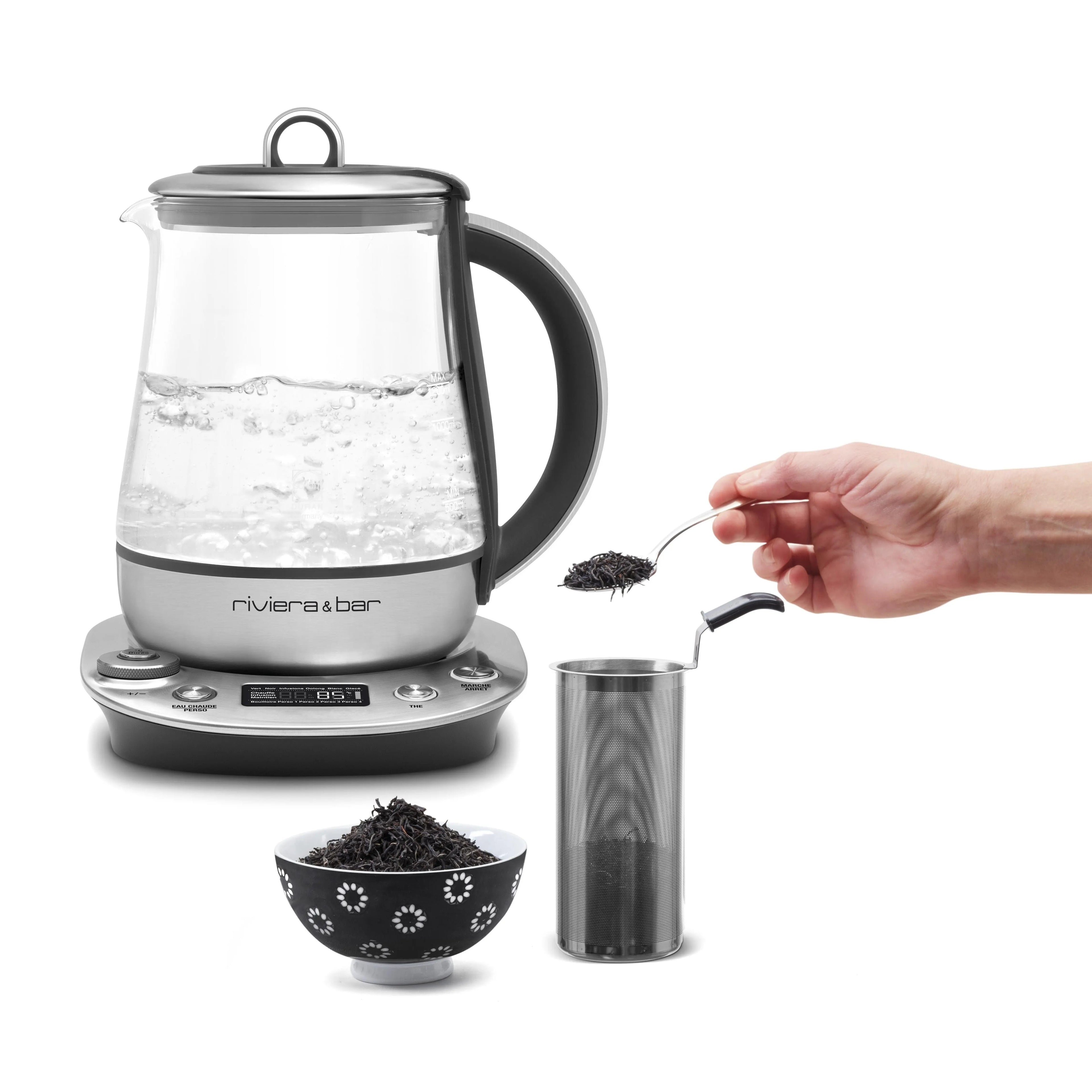 Voici quelques légendes alternatives possibles, en français :

*Bouilloire en verre Riviera & Bar avec théière en acier inoxydable et bol de thé noir.*
*Préparation du thé : Bouilloire électrique, filtre à thé et bol de thé.*
*Nature morte d'une bouilloire en verre avec de l'eau bouillante et des accessoires de préparation du thé.*